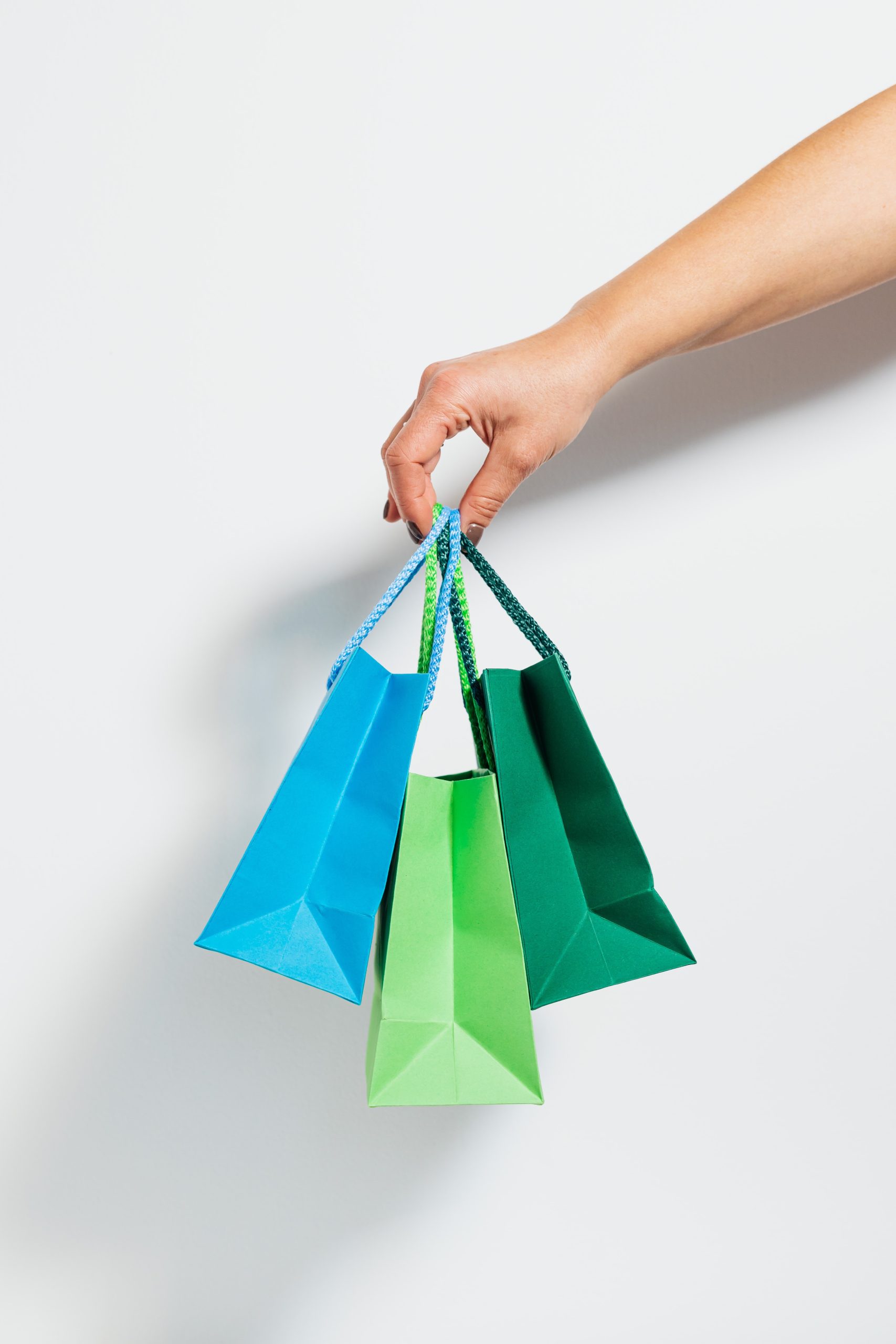 A hand holding 3 blue and green shopping bags.