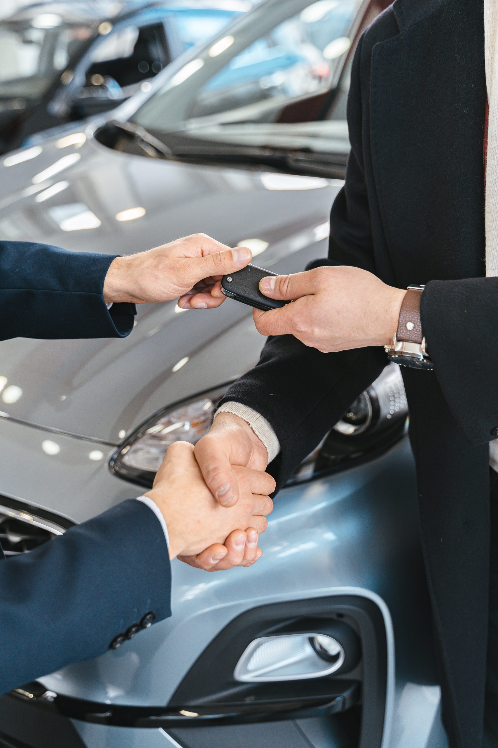 Two male presenting people shaking hands and exchanging car keys.